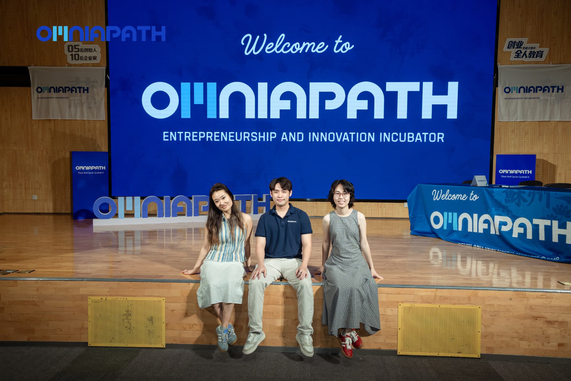 Barry Li, Founder and Chairman of OMNIAPATH, seated at the center with partners Olivia and Yeyang in front of the OMNIAPATH Entrepreneurship and Innovation Incubator screen